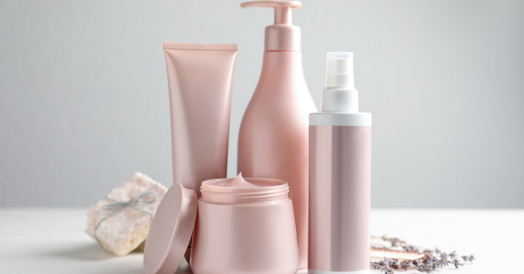 Closeup of four types of hair products in different kinds of pink and white containers sitting on a table.