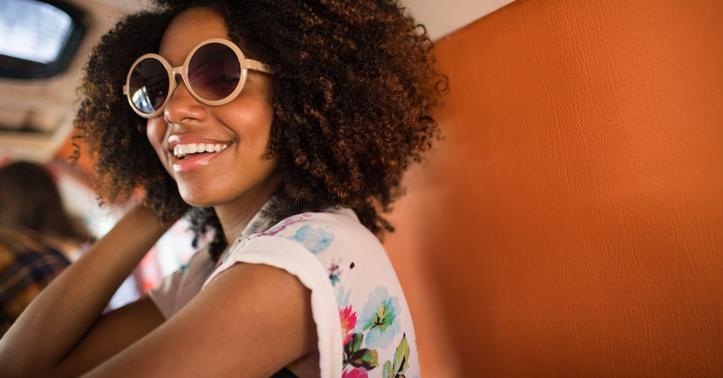 A young African American woman wearing sunglasses and resting her hand on her curly hair while sitting in a camper van.