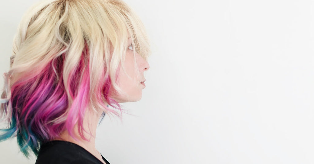 A side profile of a Caucasian woman against a white background. Her hair is dyed blue, pink, and blonde.