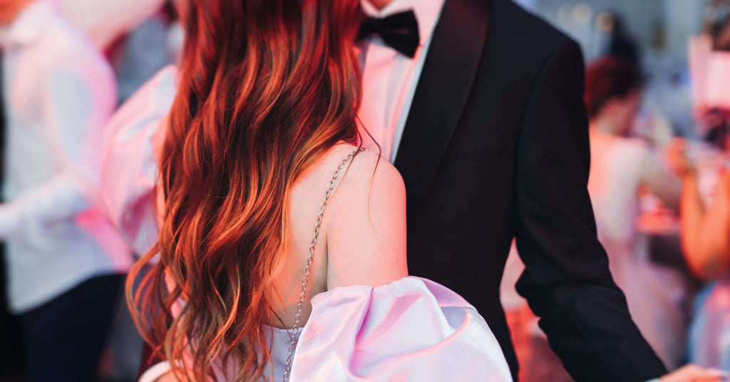 A young boy and girl, dressed elegantly for a school celebration, dance together with their faces out of view.