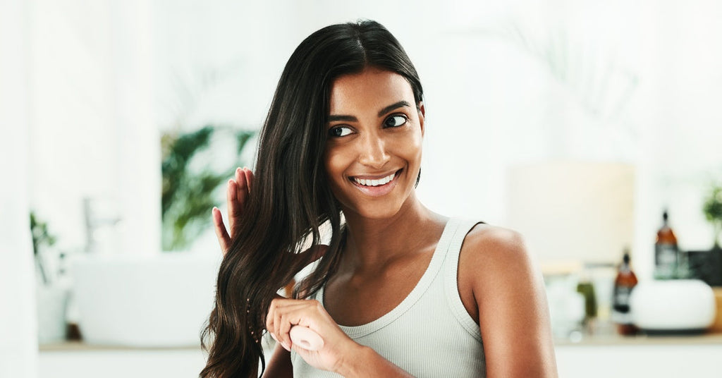 A close-up of a woman brushing her hair in the mirror. She smiles as she cares for her hair in the bathroom.
