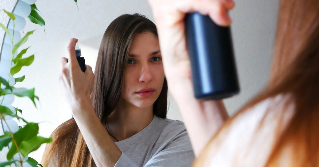A young woman gazes into a mirror, holding a can of hair spray as she gets ready to apply it to her hair.